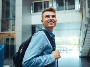 Ein Auszubildender mit Rucksack über der Schulter blickt zurück und lächelt jemanden an