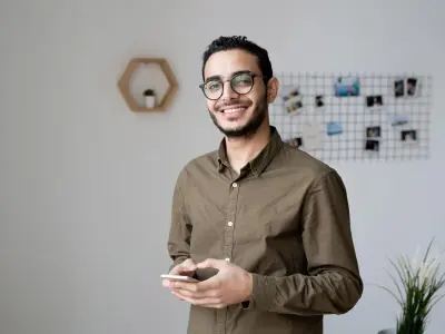 Mann mit Smartphone in der Hand lächelt in die Kamera