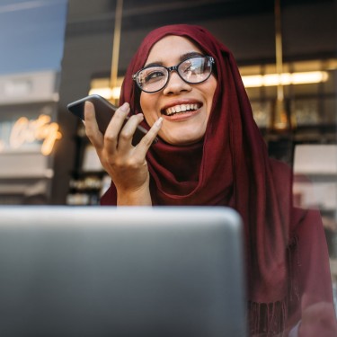 Frau sitzt vor einem Laptop und telefoniert