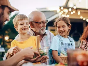 Ein Opa hat seine beiden Enkel auf dem Schoß bei einem Grillfest