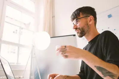 Mann sitzt mit Laptop am Schreibtisch und hält eine Tasse in der Hand