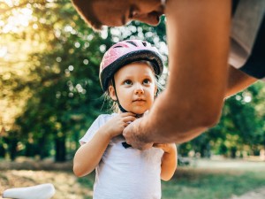 Care-Arbeit: Mann schließt den Fahrradhelm eines Kindes