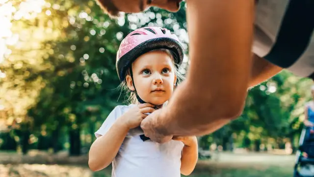 Care-Arbeit: Mann schließt den Fahrradhelm eines Kindes