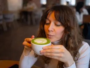 Eine Frau sitzt in einem Cafe und genießt einen Matcha-Tee.