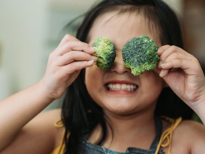Ein kleines Mädchen hält sich Brokkoli-Röschen vor die Augen und grinst