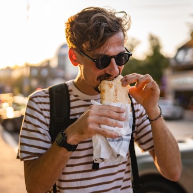 Ein junger Mann steht auf der Straße und beißt in ein Sandwich.