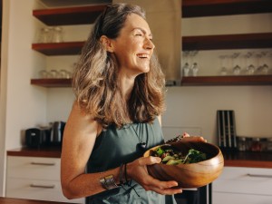Eine etwas ältere Frau hält eine Schüssel Salat in den Händen und lächelt