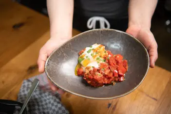 Hände zeigen eine frisch gekochte Shakshuka