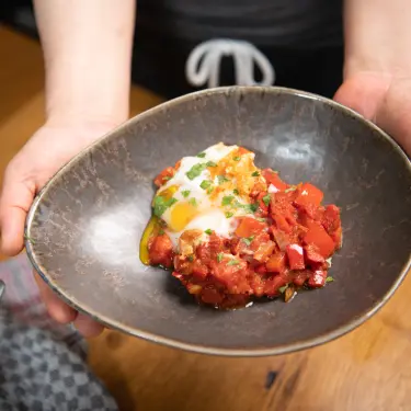Hände zeigen eine frisch gekochte Shakshuka