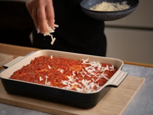 Spinat-Ricotta-Lasagne wird vor dem Backen mit Käse bestreut
