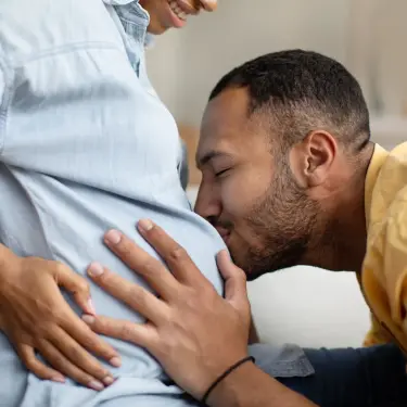 Eine Schwangere mit dem Handy in der Hand blickt zur Seite und lächelt