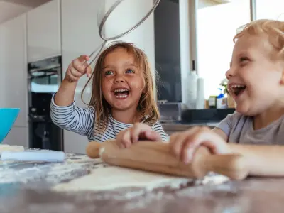 2 Kinder sind in der Küche und rollen einen Teig aus.