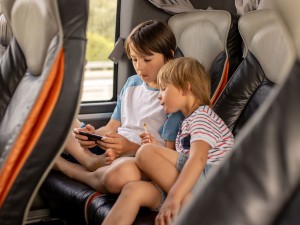 Reisen mit Kindern: 2 Kinder im Reisebus schauen auf ein Handy