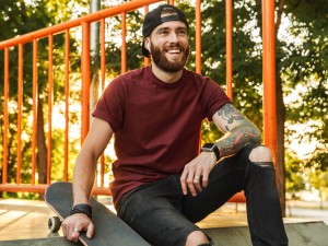 Junger Mann mit Tattoos und Skateboard