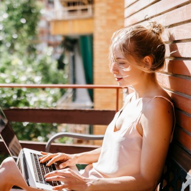 Frau sitzt am Laptop auf dem Balkon