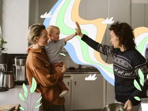 Zwei Frau mit einem Kind auf dem Arm geben sich ein High-Five in einer Küche