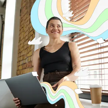 Eine junge Frau mit Kurzhaarschnitt sitze mit Laptop auf der Fensterbank eines Büros