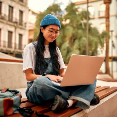 Junge Frau sitzt draußen am Laptop