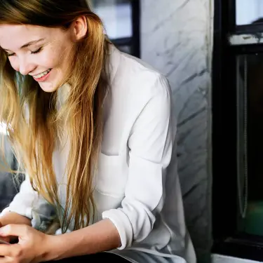 Eine junge Frau hält ihr Smartphone in der Hand und lächelt