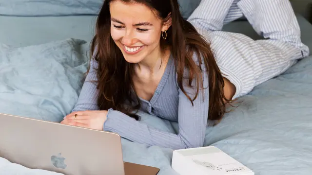 Eine Frau liegt mit einem Laptop auf dem Bett