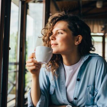 Frau hält eine Tasse in der Hand und schaut aus dem Fenster