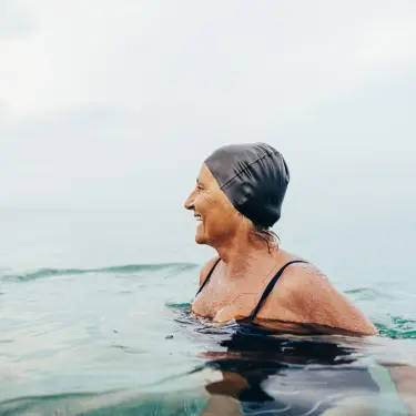 Eine ältere Frau schwimmt in einem See und lacht