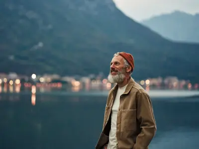Ein Mann steht in den Bergen am See und schaut lächelnd in die Ferne.