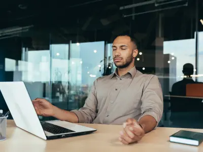 Ein Mann sitzt vor seinem Laptop und führt eine Entspannungsübung durch