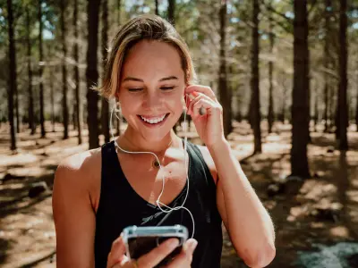 Eine Frau ist zum Joggen im Wald und schaut lächelnd auf ihr Handy
