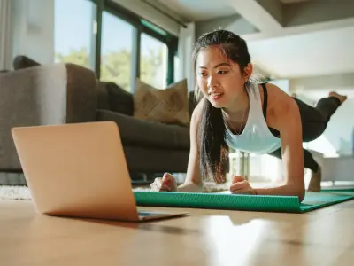 Eine junge Frau macht zuhause vor dem Laptop auf einer Yoga-Matte eine Plank
