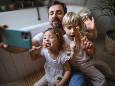 Ein Vater macht ein Selfie von seinen 2 Kindern und Zahnbürsten in den Händen