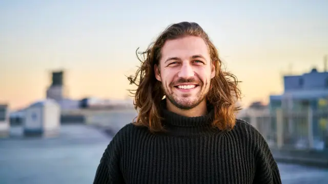 Ein junger Mann mit längeren Haaren lächelt in die Kamera