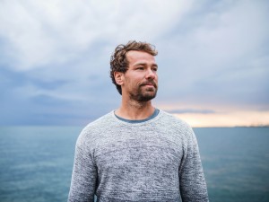 Mann steht vor einem Gewässer und schaut in die Ferne