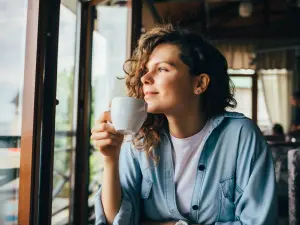 Eine Frau hält eine Tasse in der Hand und schaut aus dem Fenster