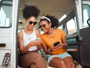 Zwei Frauen sitzen im offenen Auto und schauen gemeinsam in ihre Smartphones