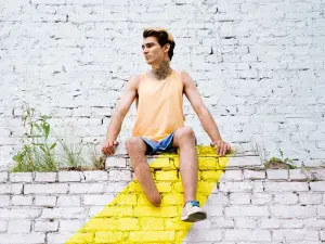 Junger Mann sitzt auf einer Mauer und schaut zur Seite