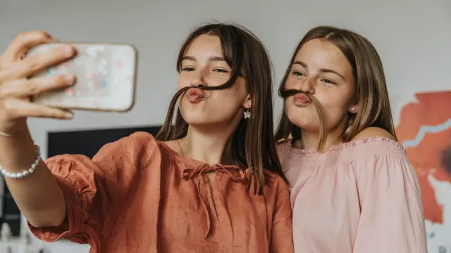Zwei Mädchen mit Haarsträhne als Schnauzbart machen ein Selfie