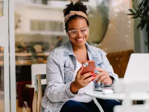 Eine Frau sitzt im Cafe mit Laptop und schaut auf ihr Smartphone
