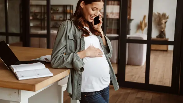 Eine schwangere Frau steht in einem Raum und telefoniert.